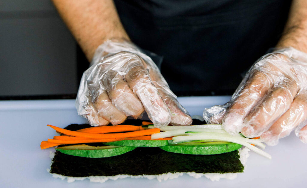 A pair of hands wearing gloves preparing sushi